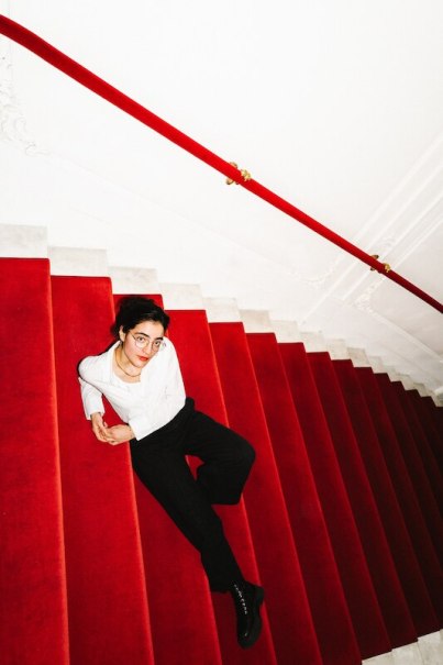 Eine Person in einem wei&szlig;en Hemd und schwarzer Hose liegt entspannt auf einer roten Treppe mit einem roten Gel&auml;nder., &copy; Rosenau Kultur e.V.