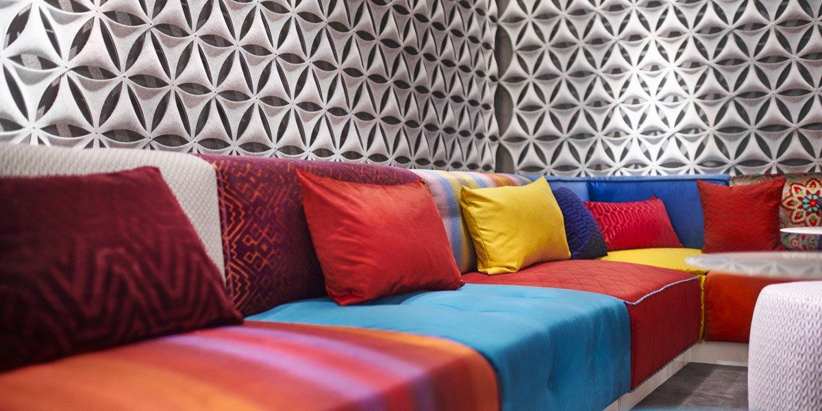 Colorful sofas with red, yellow and blue cushions in front of a geometrically patterned wallpaper in a lobby., © Jaz Hotel Stuttgart Colorful sofas with red, yellow and blue cushions in front of a geometrically patterned wallpaper in a lobby., © Jaz Hotel Stuttgart