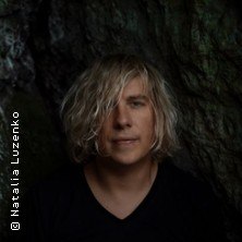 Person with blond, wavy hair in front of a dark, rocky background. The atmosphere is mystical and natural., &copy; see on the left