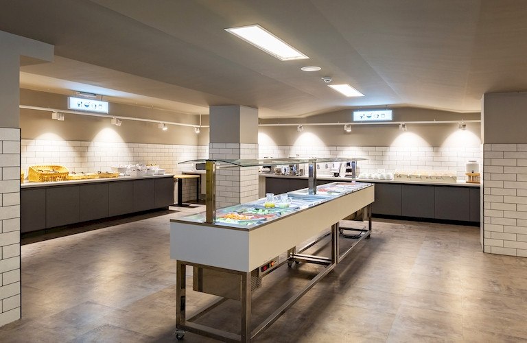 Ein modernes Frühstücksbuffet in einem hellen Raum mit Fliesenwänden und mehreren Essensstationen., © A&O Hostels Marketing GmbH