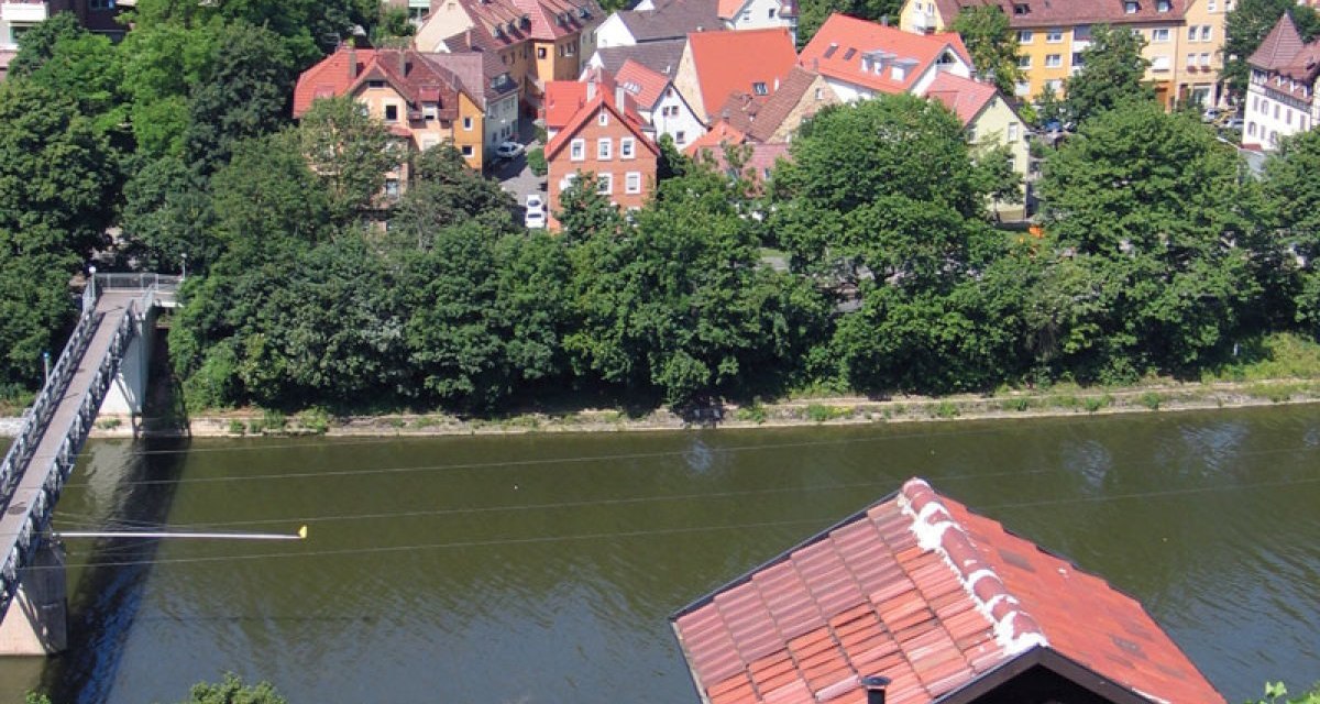 View of the Neckar with a bridge, surrounded by green trees and red roofs of houses in the background., © Stuttgart-Marketing GmbH View of the Neckar with a bridge, surrounded by green trees and red roofs of houses in the background., © Stuttgart-Marketing GmbH