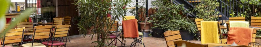 Cozy outdoor caf&eacute; area with wooden tables and chairs, surrounded by plants. Colorful blankets on the chairs create an inviting atmosphere., &copy; SMG, Sarah Schmid