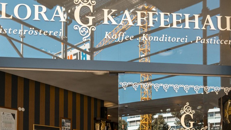 Eingang des Glora Kaffeehauses mit dekorativem Schriftzug auf der Glasfront. Im Hintergrund sind Baukräne zu sehen., © SMG, Sarah Schmid