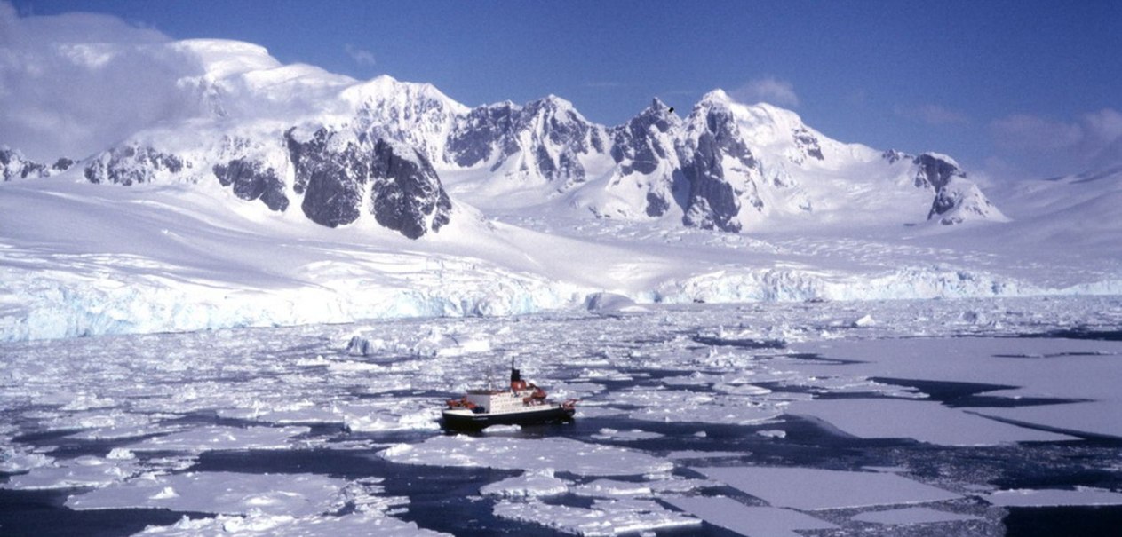 Ein Schiff fährt durch das Eis in der Antarktis, umgeben von schneebedeckten Bergen und einer eisigen Landschaft., © Bluemel