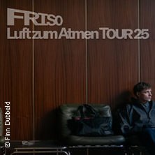 Person sitzt auf einem Sofa vor einer Holzwand. Oben steht 'FRISO Luft zum Atmen TOUR 25'., © links im Bild