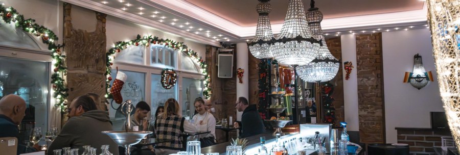 Festlich dekorierte Bar mit Kronleuchtern, Gästen an der Theke und weihnachtlichem Schmuck. Gläser und Flaschen stehen auf der Theke., © SMG Stuttgart Marketing GmbH - Sarah Schmid