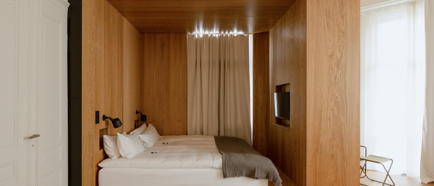 Ein modernes Schlafzimmer mit einem Holzkubus, der ein Bett und einen Fernseher enthält. Der Raum ist hell und minimalistisch gestaltet., © Peter Oliver Wolff / DAS EDITH