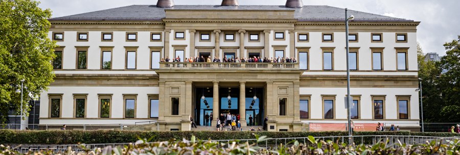 The Stadtpalais - Museum f&uuml;r Stuttgart, a classicist building with people on the balcony, surrounded by trees and hedges., &copy; @ die arge lola / Kai Loges + Andreas Langen