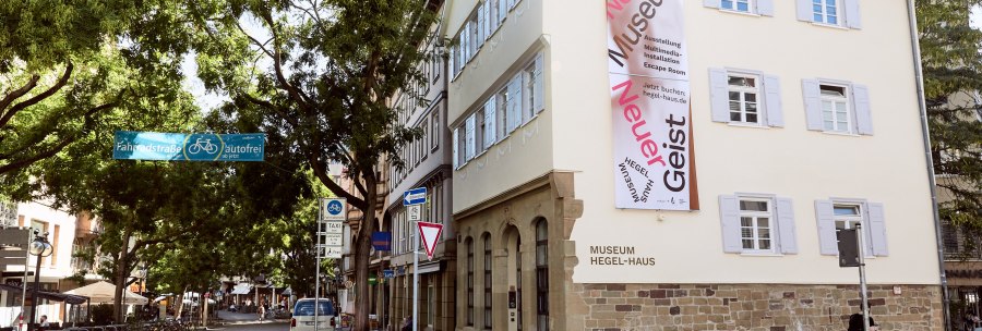 Das Hegel-Haus in Stuttgart mit einem großen Banner an der Fassade. Die Straße davor ist autofrei und von Bäumen gesäumt., © Julia Ochs