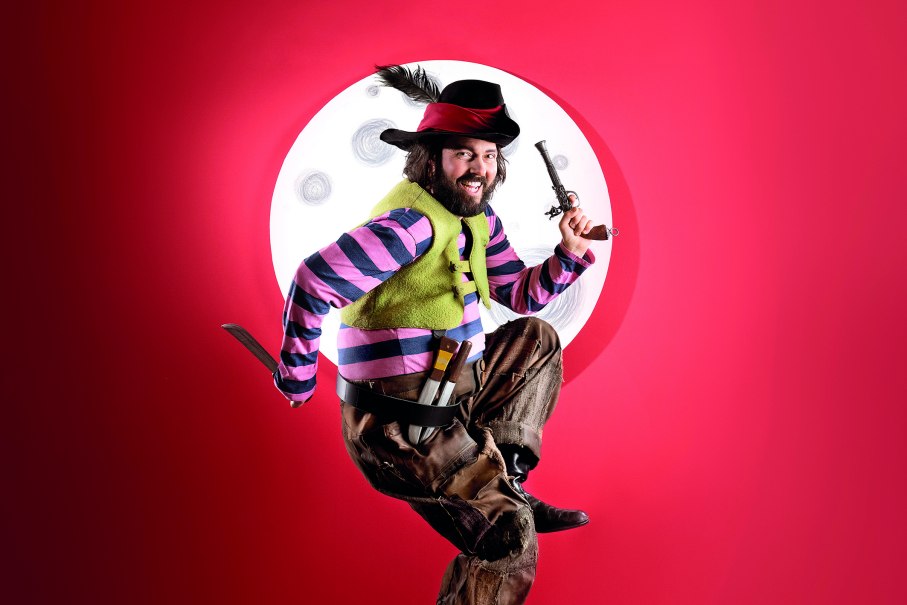 Person in bunter Piratenkleidung springt vor einem roten Hintergrund mit einem Mond im Hintergrund. Sie hält eine Pistole und ein Messer., © Martin Sigmund Person in bunter Piratenkleidung springt vor einem roten Hintergrund mit einem Mond im Hintergrund. Sie hält eine Pistole und ein Messer., © Martin Sigmund