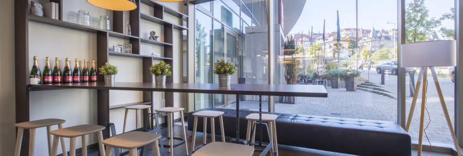 Modern lobby with high tables, stools and large lamps. In the background are shelves with decorations and a window front with a view to the outside., © Park Inn by Radisson Stuttgart Modern lobby with high tables, stools and large lamps. In the background are shelves with decorations and a window front with a view to the outside., © Park Inn by Radisson Stuttgart