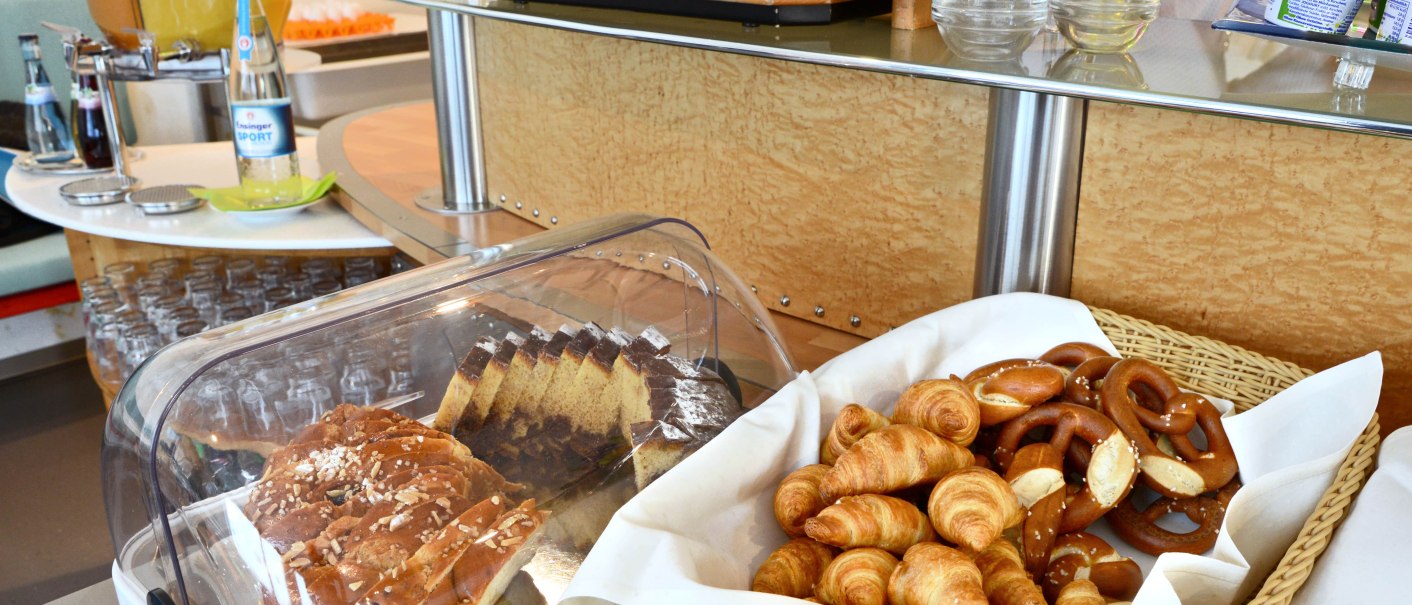 Ein Frühstücksbuffet mit Croissants, Brezeln, Kuchen, Marmeladen und Getränken wie Wasser und Saft., © Abalon Hotel Ideal Ein Frühstücksbuffet mit Croissants, Brezeln, Kuchen, Marmeladen und Getränken wie Wasser und Saft., © Abalon Hotel Ideal