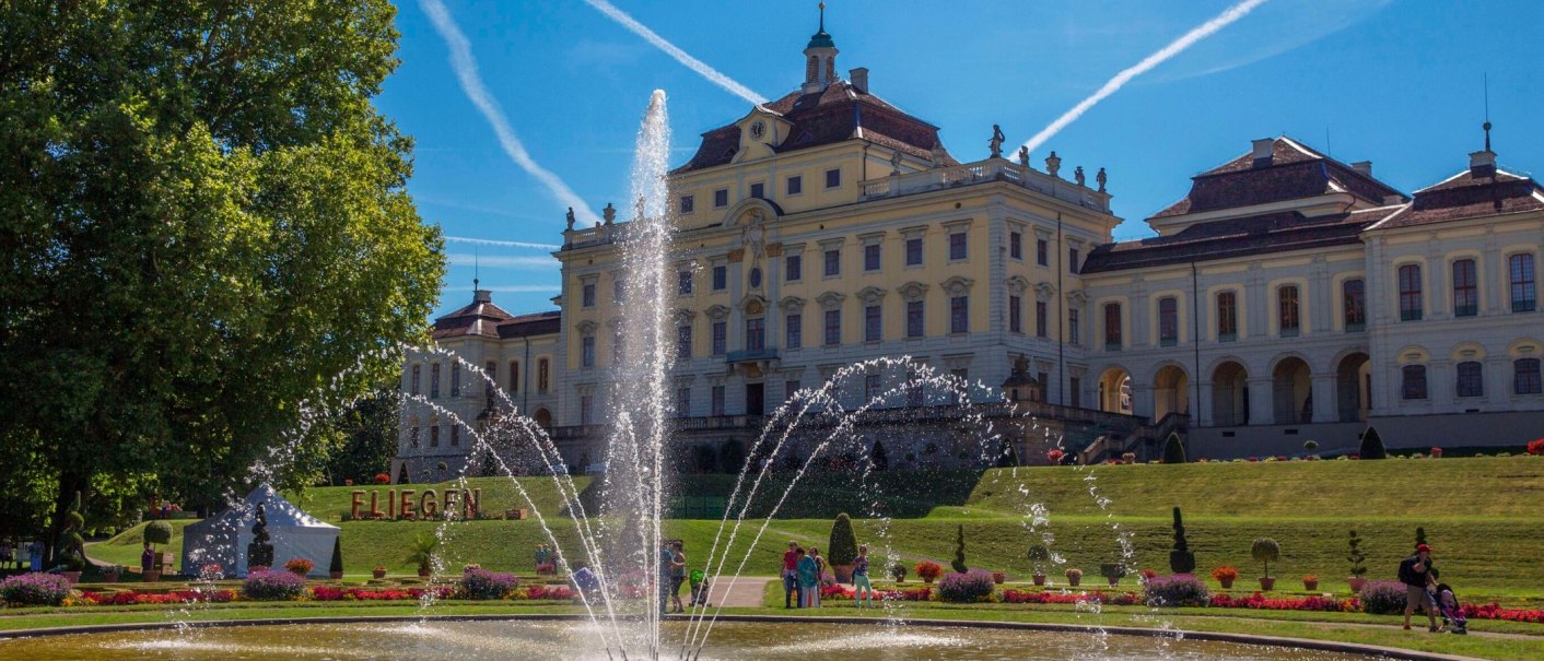 The Ludwigsburg Residential Palace with a large fountain in the foreground. The sky is blue with contrails, surrounded by manicured gardens., © Tourismus & Events Ludwigsburg The Ludwigsburg Residential Palace with a large fountain in the foreground. The sky is blue with contrails, surrounded by manicured gardens., © Tourismus & Events Ludwigsburg