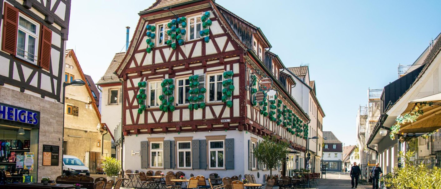 Half-timbered house in Kirchheim unter Teck with green shutters. In front of the building are tables and chairs from a street café., © Stuttgart-Marketing GmbH, Sarah Schmid