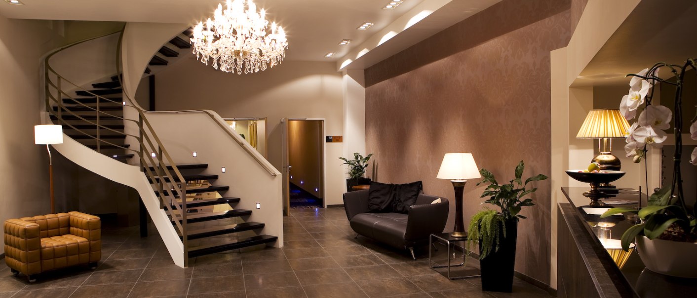Elegantes Foyer mit Wendeltreppe, Kronleuchter, Ledersesseln und Pflanzen. Die Beleuchtung schafft eine warme Atmosphäre., © Ross Messehotel Elegantes Foyer mit Wendeltreppe, Kronleuchter, Ledersesseln und Pflanzen. Die Beleuchtung schafft eine warme Atmosphäre., © Ross Messehotel