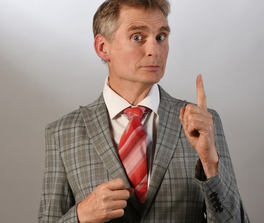 Ein Mann im grauen karierten Anzug und roter Krawatte hebt den Zeigefinger, als ob er etwas betonen möchte. Hintergrund ist neutral., © Rosenau Kultur e.V. Ein Mann im grauen karierten Anzug und roter Krawatte hebt den Zeigefinger, als ob er etwas betonen möchte. Hintergrund ist neutral., © Rosenau Kultur e.V.