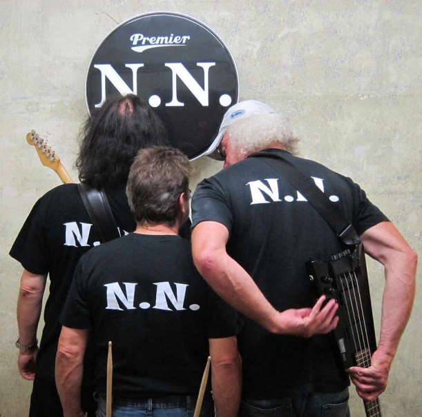 Drei Personen mit schwarzen 'N.N.'-T-Shirts stehen vor einer Trommel mit dem gleichen Logo. Sie halten Instrumente., © NNBros