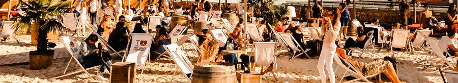 Beach bar with sun loungers and parasols, surrounded by palm trees. People relax under a blue sky with clouds., © Sky Beach