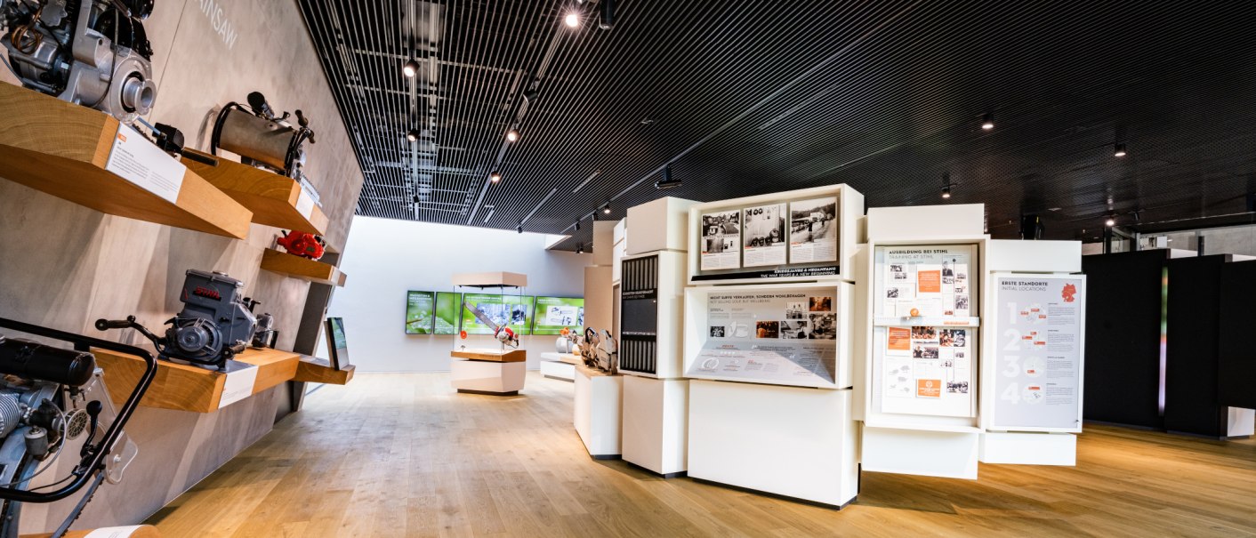 A modern exhibition featuring historic STIHL machines and informational displays. A bright, open layout with wood and metal elements., © STIHL Markenwelt A modern exhibition featuring historic STIHL machines and informational displays. A bright, open layout with wood and metal elements., © STIHL Markenwelt