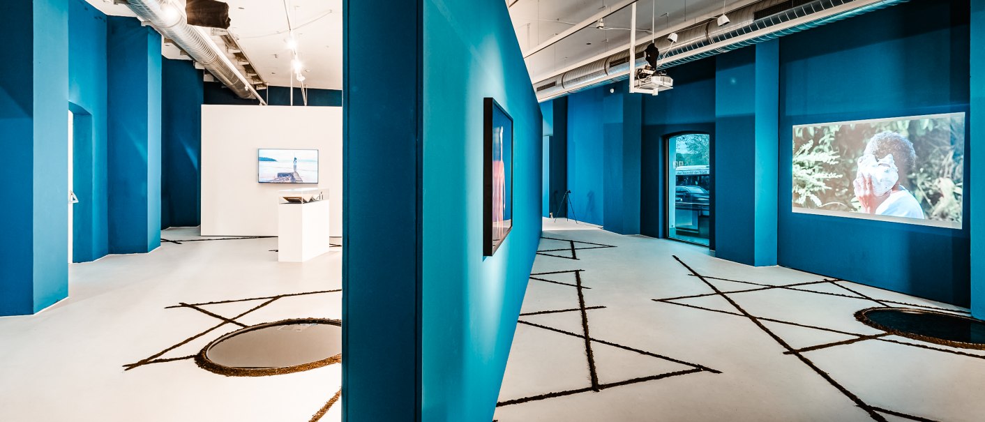 Moderne Galerie mit blauen W&auml;nden, Videoinstallationen und geometrischen Mustern auf dem Boden. Industrielles Design mit sichtbaren L&uuml;ftungsrohren., &copy; Ifa Galerie Stuttgart