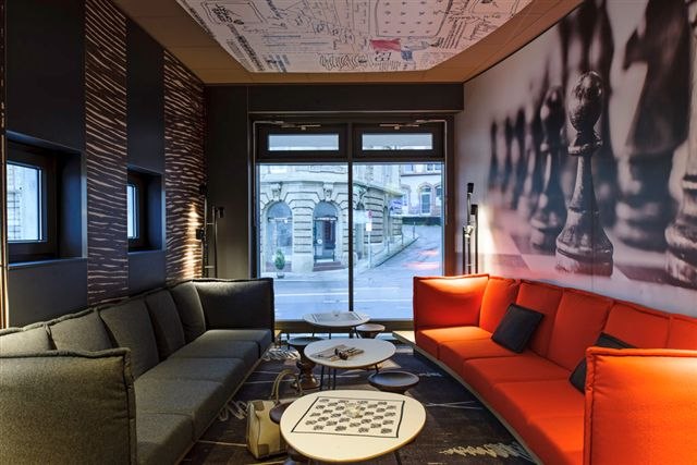 Modern room with gray and red sofas, chessboard pattern on table, wall with chess pieces, window with view of building., &copy; TOMAS