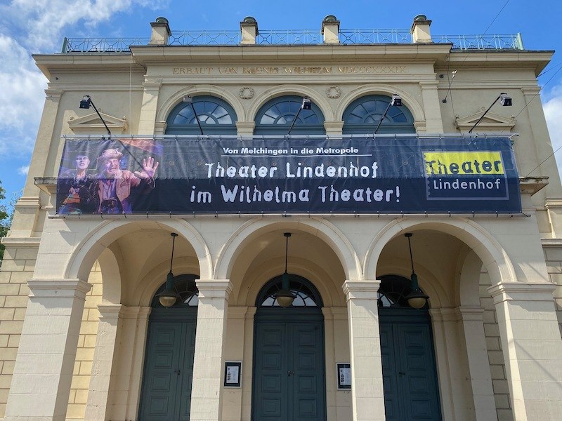 Fassade des Wilhelma Theaters mit einem großen Banner des Theater Lindenhof. Der Schriftzug lautet: 'Von Melchingen in die Metropole'., © Wilhelma Theater