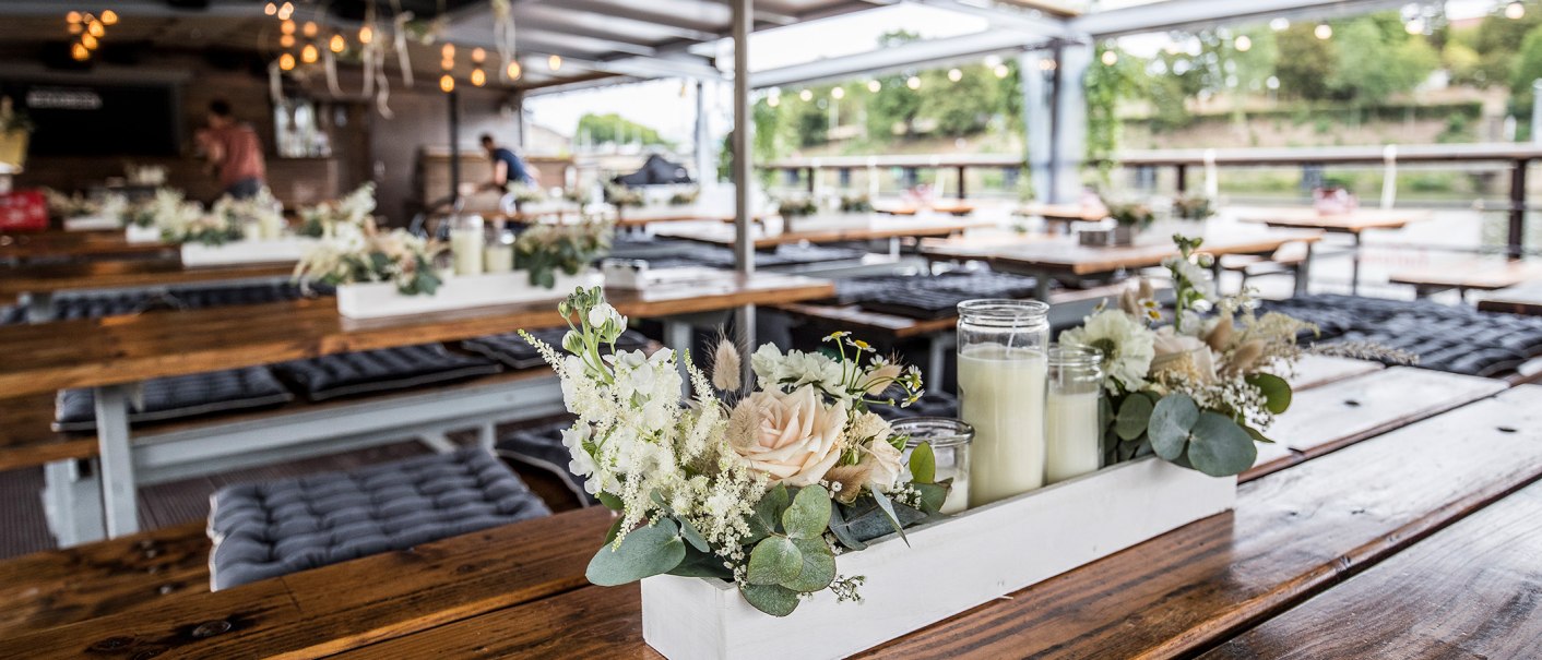 Interior of a restaurant with wooden tables, flower arrangements and candles. Lights and a person can be seen in the background., © all copyrights are reserved by maks richter Interior of a restaurant with wooden tables, flower arrangements and candles. Lights and a person can be seen in the background., © all copyrights are reserved by maks richter