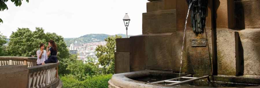 The Galatea Fountain on Eugensplatz in Stuttgart. Two people are sitting on a balustrade, with the city and green hills in the background., &copy; Stuttgart-Marketing GmbH Christoph D&uuml;pper