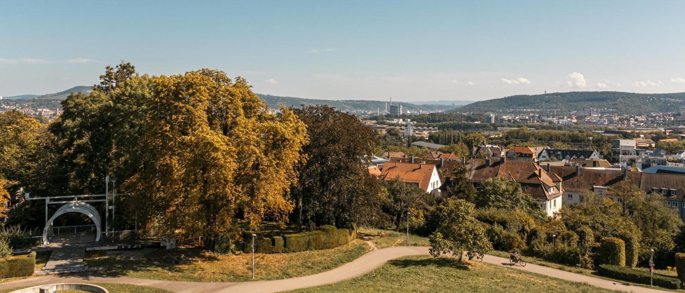 Blick über den Leibfriedschen Garten auf eine Stadt mit herbstlichen Bäumen, Häusern und Hügeln im Hintergrund unter klarem Himmel., © Stuttgart Marketing GmbH, Sarah Schmid