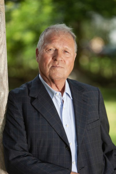An older man in a checked suit leans against a tree trunk. The background is blurred and green, indicating an outdoor shot., &copy; Renitenztheater Stuttgart e.V.