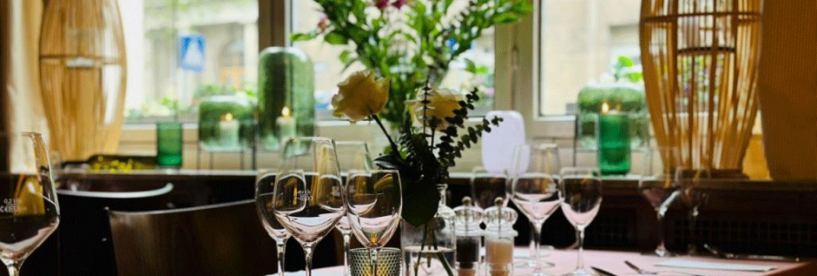 A stylishly laid table in a café with wine glasses, cutlery and flower arrangements in front of a window., © FreCla Gastronomiebetriebe GmbH