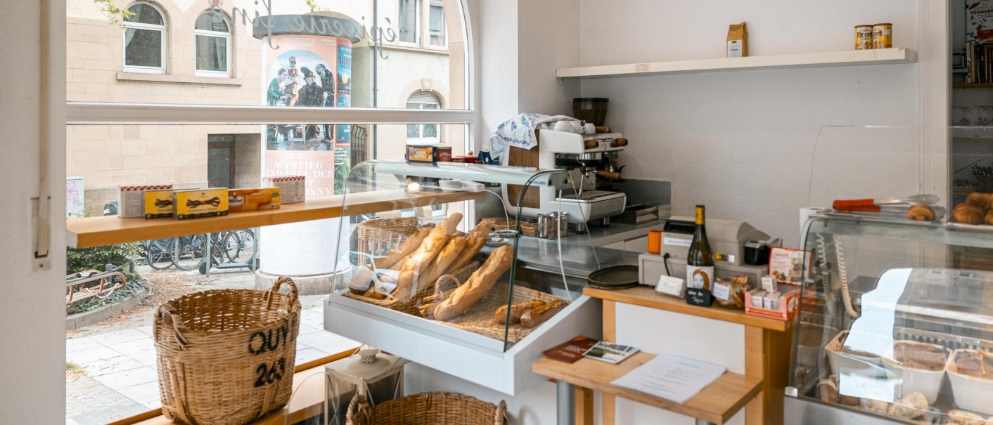 Ein kleiner Feinkostladen mit Baguettes und Croissants in Vitrinen. Im Hintergrund sind eine Kaffeemaschine und ein Fenster mit Blick nach draußen., © SMG, Sarah Schmid