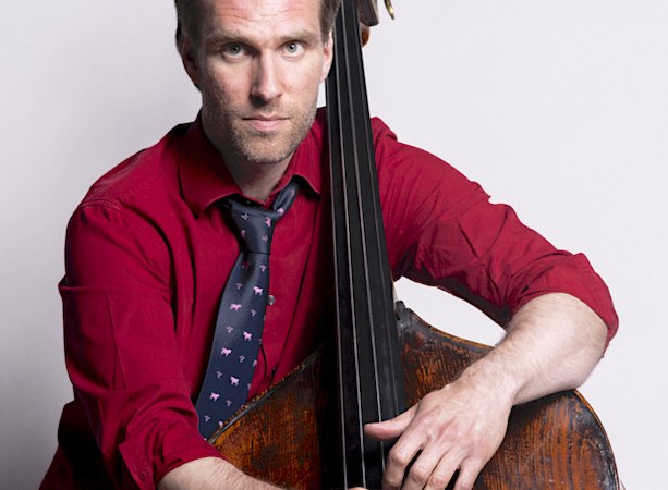 Ein Mann in rotem Hemd und Krawatte spielt einen Kontrabass. Er hält den Bogen in der rechten Hand und schaut in die Kamera., © Staatliche Hochschule für Musik und Darstellende Kunst Ein Mann in rotem Hemd und Krawatte spielt einen Kontrabass. Er hält den Bogen in der rechten Hand und schaut in die Kamera., © Staatliche Hochschule für Musik und Darstellende Kunst