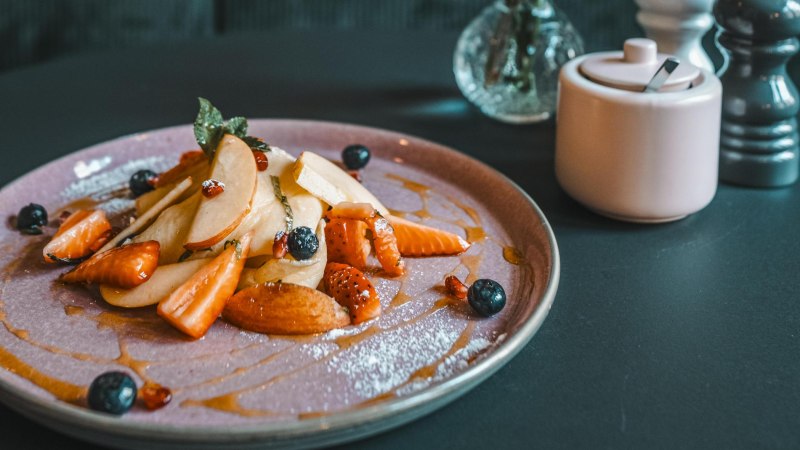 Ein Teller mit geschnittenen Früchten, Beeren und Sirup. Daneben eine Zuckerdose und ein Salzstreuer auf einem dunklen Tisch., © Lupin, Stuttgart
