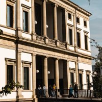 A historic building with columns and large windows, surrounded by trees. People walk on a path along the fa&ccedil;ade., &copy; SMG Stuttgart Marketing GmbH - Sarah Schmid