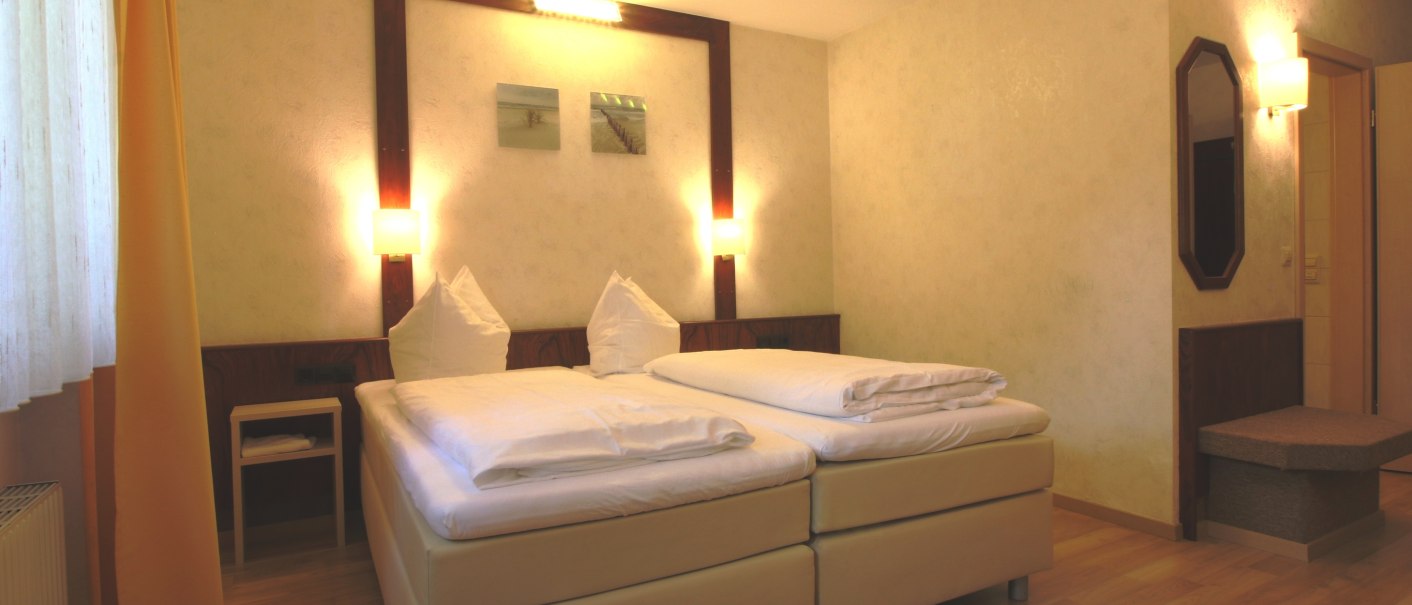 Gemütliches Doppelzimmer mit zwei Betten, Nachttisch, Wandlampen und Spiegel. Helle Vorhänge und Holzboden schaffen eine einladende Atmosphäre., © TOMAS Gemütliches Doppelzimmer mit zwei Betten, Nachttisch, Wandlampen und Spiegel. Helle Vorhänge und Holzboden schaffen eine einladende Atmosphäre., © TOMAS