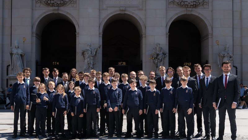 Gruppe von Jungen und Männern in blauen Pullovern vor einem historischen Gebäude mit Säulen und Statuen., © Knabenchor collegium iuvenum Stuttgart