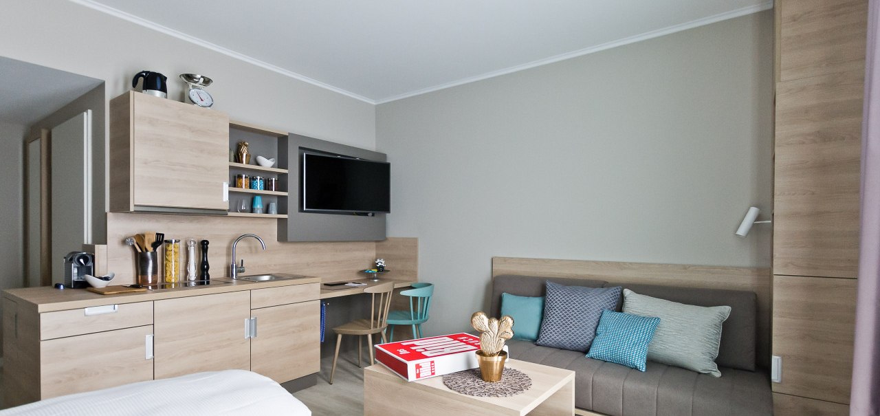 Moderne Einzimmerwohnung mit K&uuml;chenzeile, Sofa, Fernseher und Esstisch. Helle Holzm&ouml;bel und neutrale Farben dominieren den Raum., &copy; Arthotel Ana / elaya