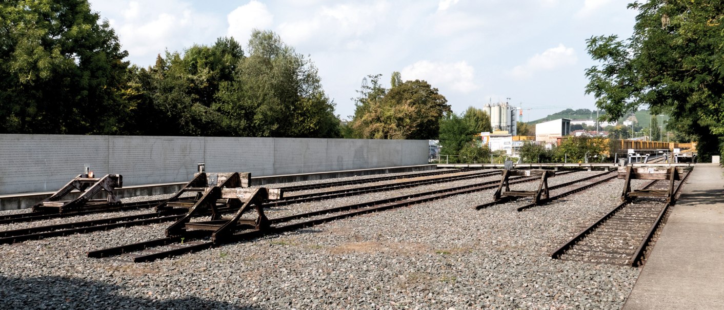 Gedenkst&auml;tte mit stillgelegten Bahngleisen, umgeben von B&auml;umen und einer Mauer. Ein ruhiger Ort des Erinnerns., &copy; Foto-Kunst Andreas Keller