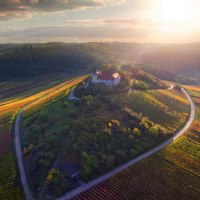 Aerial view of Michaelsberg, surrounded by colorful vineyards at sunset. A church stands on the hill, surrounded by woods and fields., © Neckar-Zaber-Tourismus e.V