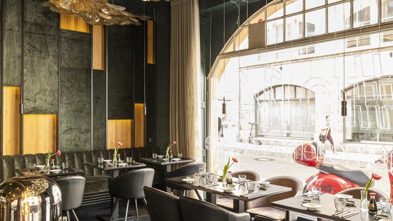 Elegantes Restaurant mit modernen Möbeln, großen Fenstern und stilvoller Dekoration. Draußen sind rote Motorroller zu sehen., © Stuttgart-Marketing GmbH, Sarah Schmid