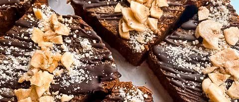 Bananenbrotstücke mit Schokoladenglasur und Bananenchips dekoriert, auf einem weißen Hintergrund präsentiert., © wyld Stuttgart