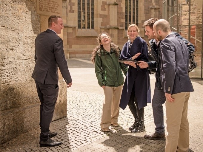 Fünf Personen lachen und interagieren vor einem historischen Gebäude. Eine Person hält ein Tablet. Es scheint eine Teamaktivität zu sein., © ExitGames Stuttgart Fünf Personen lachen und interagieren vor einem historischen Gebäude. Eine Person hält ein Tablet. Es scheint eine Teamaktivität zu sein., © ExitGames Stuttgart