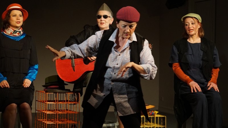 Eine Gruppe von vier Personen auf einer B&uuml;hne. Eine Person spielt Gitarre, eine tanzt, zwei sitzen. Alle tragen bunte H&uuml;te und Kost&uuml;me., &copy; Katja Ritter