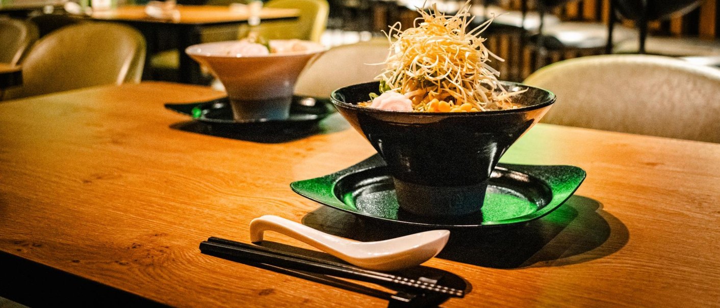 Zwei Schalen mit asiatischem Essen auf einem Holztisch, begleitet von Essstäbchen und einem Löffel., © Stuttgart Marketing GmbH - Sarah Schmid