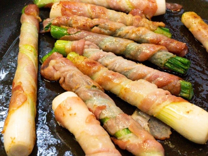 Leek sticks, wrapped in bacon, fry in a pan. The golden brown crust indicates a crispy texture., © Kultweine-Kochwelten-Kunstücke - Kochschule Sonja Lenz Leek sticks, wrapped in bacon, fry in a pan. The golden brown crust indicates a crispy texture., © Kultweine-Kochwelten-Kunstücke - Kochschule Sonja Lenz