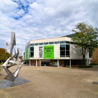 Moderne Skulptur vor dem Schauspielhaus mit großen Fenstern und Plakaten für 'Italienische Nacht'. Wolkenbedeckter Himmel, Bäume und Baukräne im Hintergrund., © Björn Klein Moderne Skulptur vor dem Schauspielhaus mit großen Fenstern und Plakaten für 'Italienische Nacht'. Wolkenbedeckter Himmel, Bäume und Baukräne im Hintergrund., © Björn Klein