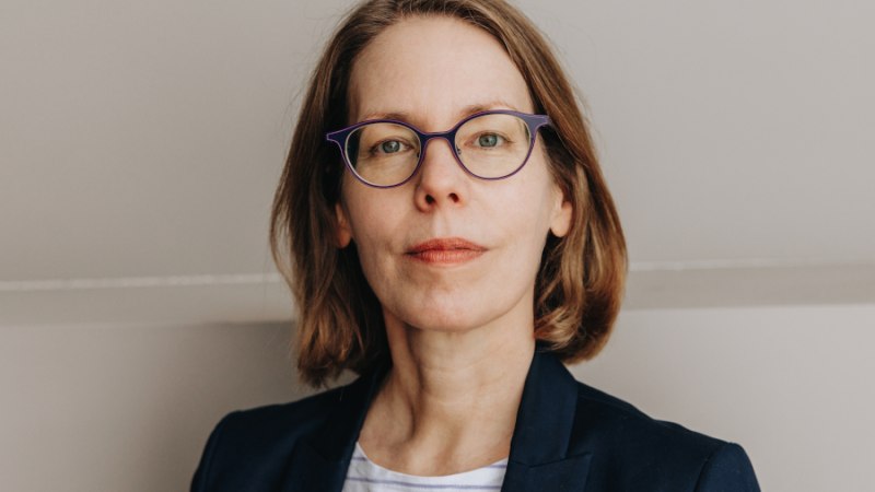 Frau mit Brille und braunen Haaren trägt einen Blazer und ein gestreiftes Shirt. Sie blickt direkt in die Kamera vor neutralem Hintergrund., © Foto: Finanzwende Felix Brüggemann