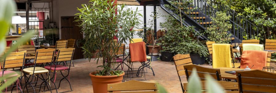 Cozy outdoor caf&eacute; area with wooden tables and chairs, surrounded by plants. Colorful blankets on the chairs create an inviting atmosphere., &copy; SMG, Sarah Schmid