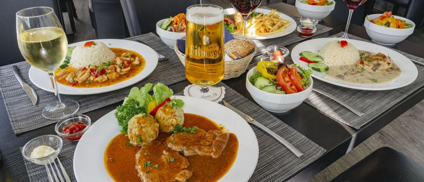 A table with various dishes: Meat with sauce, rice dishes, salads. Drinks such as beer and wine are also on display., © Plaza INN Stuttgart-Filderstadt A table with various dishes: Meat with sauce, rice dishes, salads. Drinks such as beer and wine are also on display., © Plaza INN Stuttgart-Filderstadt